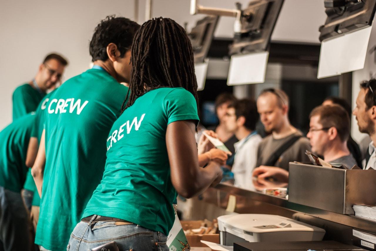 Staff at a ticket desk wearing green t-shirts that say crew on them