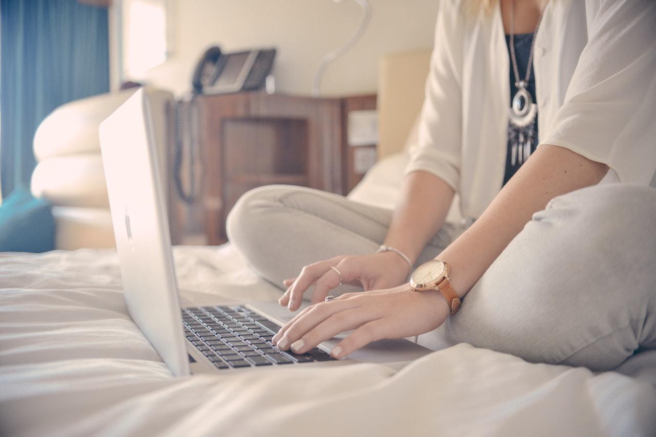 Woman writing on a laptop on a hotel bed
