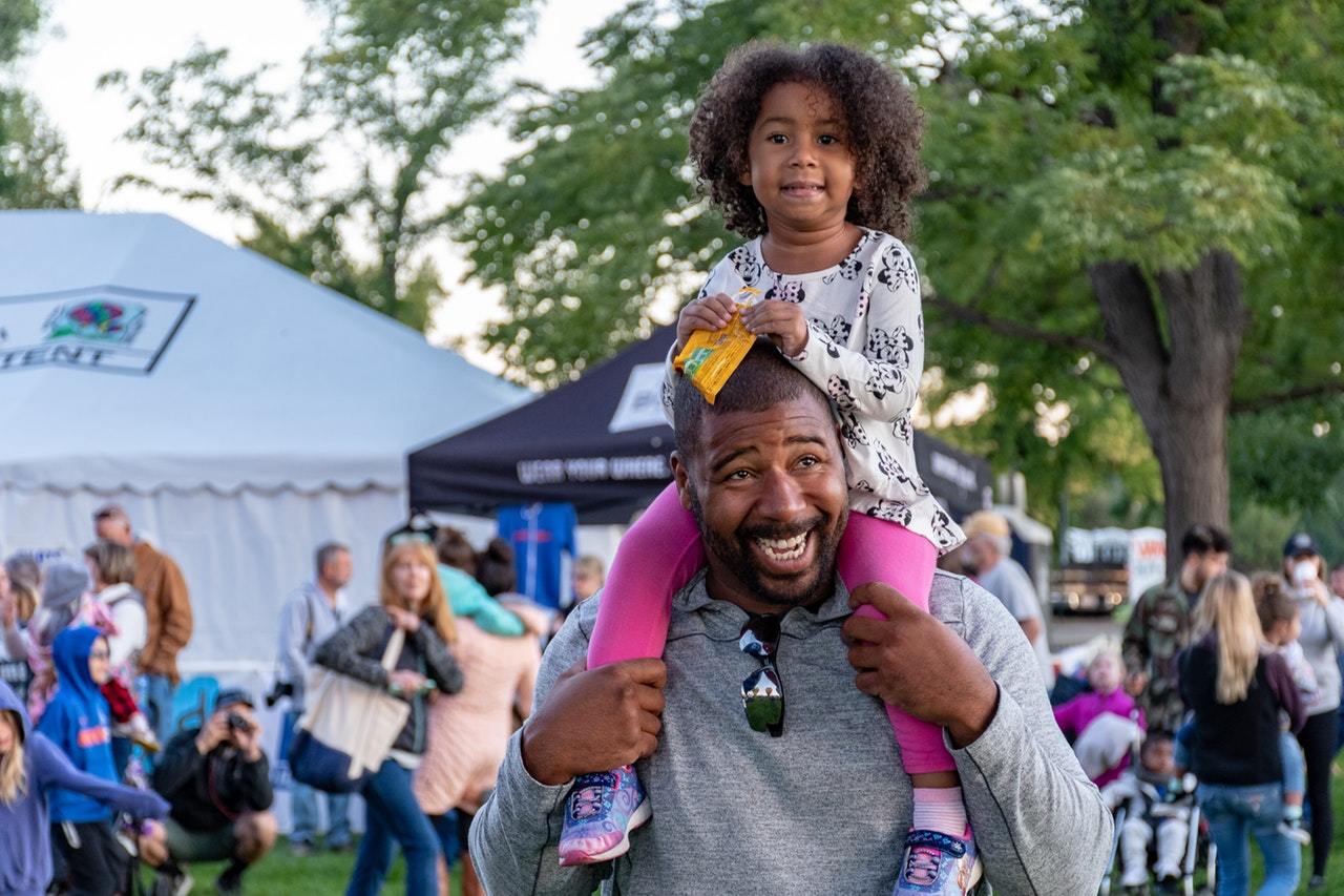 A man carry his daughter on his shoulders at a festival