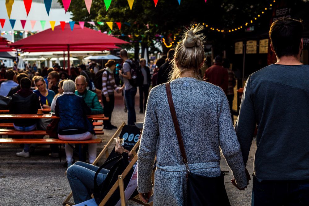 A man and woman walking through an outdoor city area with seating and sun umbrellas
