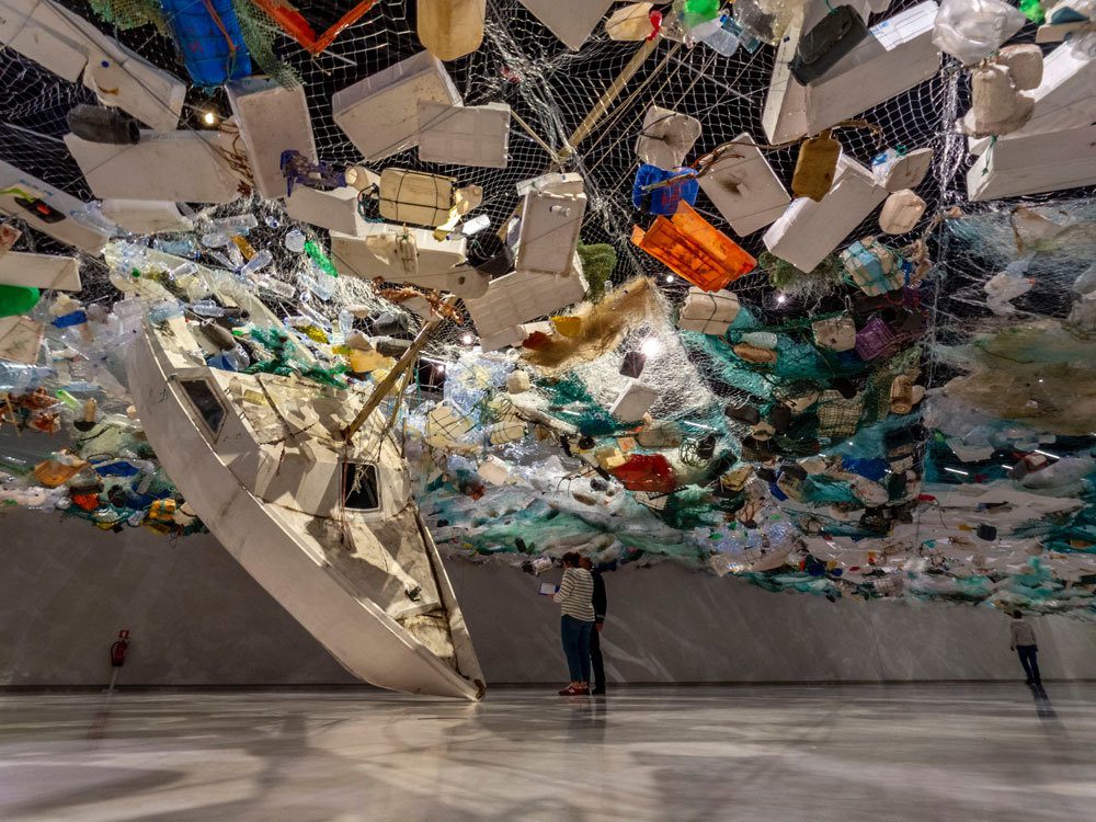 Visitors in a gallery walking under artwork made of recycled materials