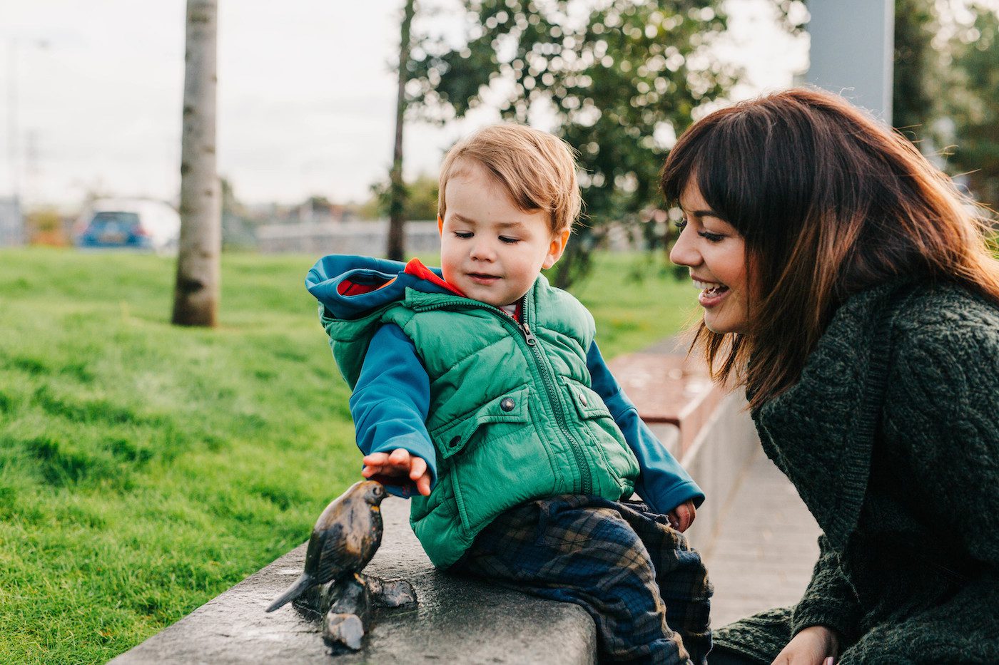 Boy and mother looking at a small public sculpture of a bird