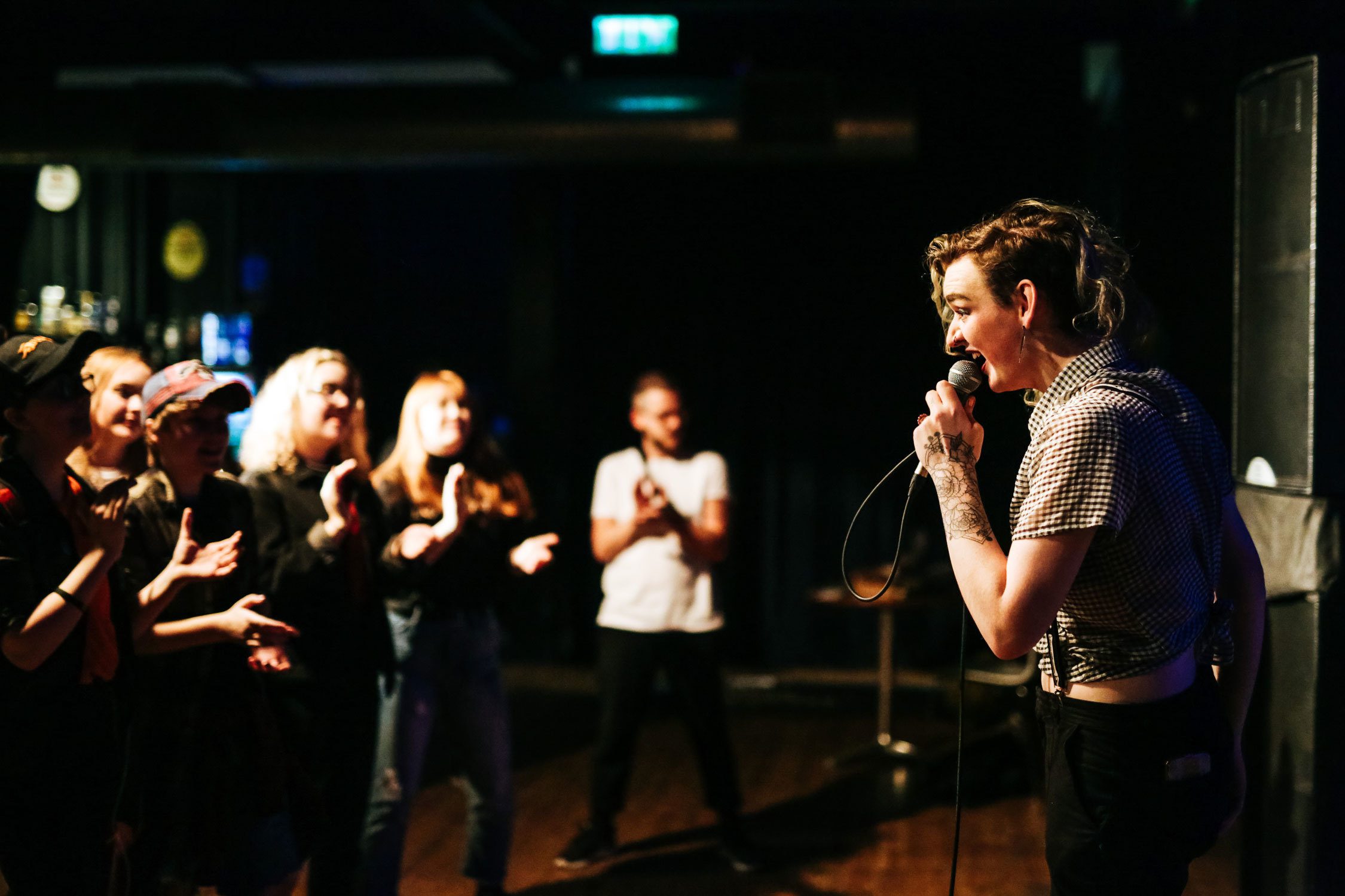 A woman speaking into a mic in front of a crowd at Outburst Queer Arts Festival