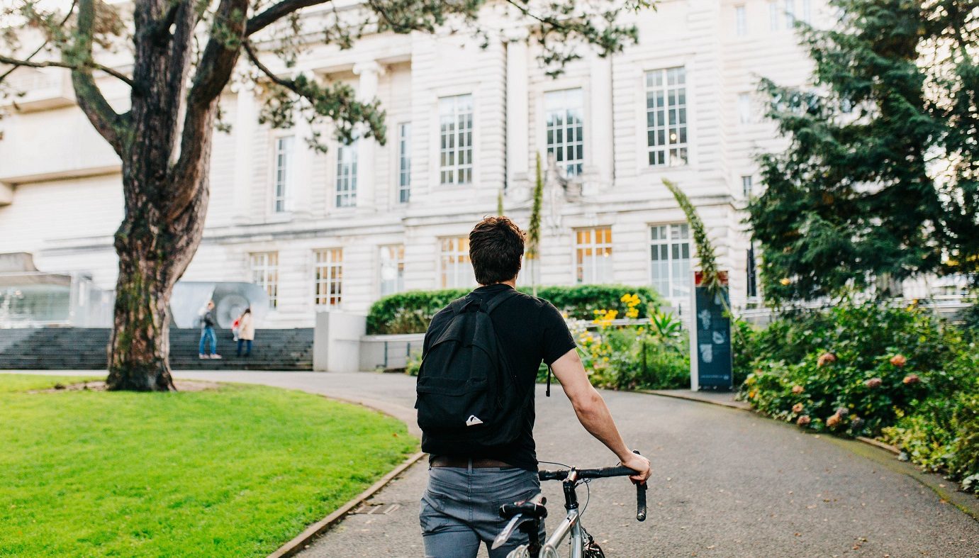Man walking bike toward a museum building