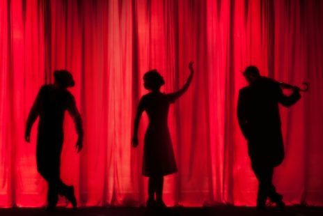 Silhouette of performers in front of a red curtain