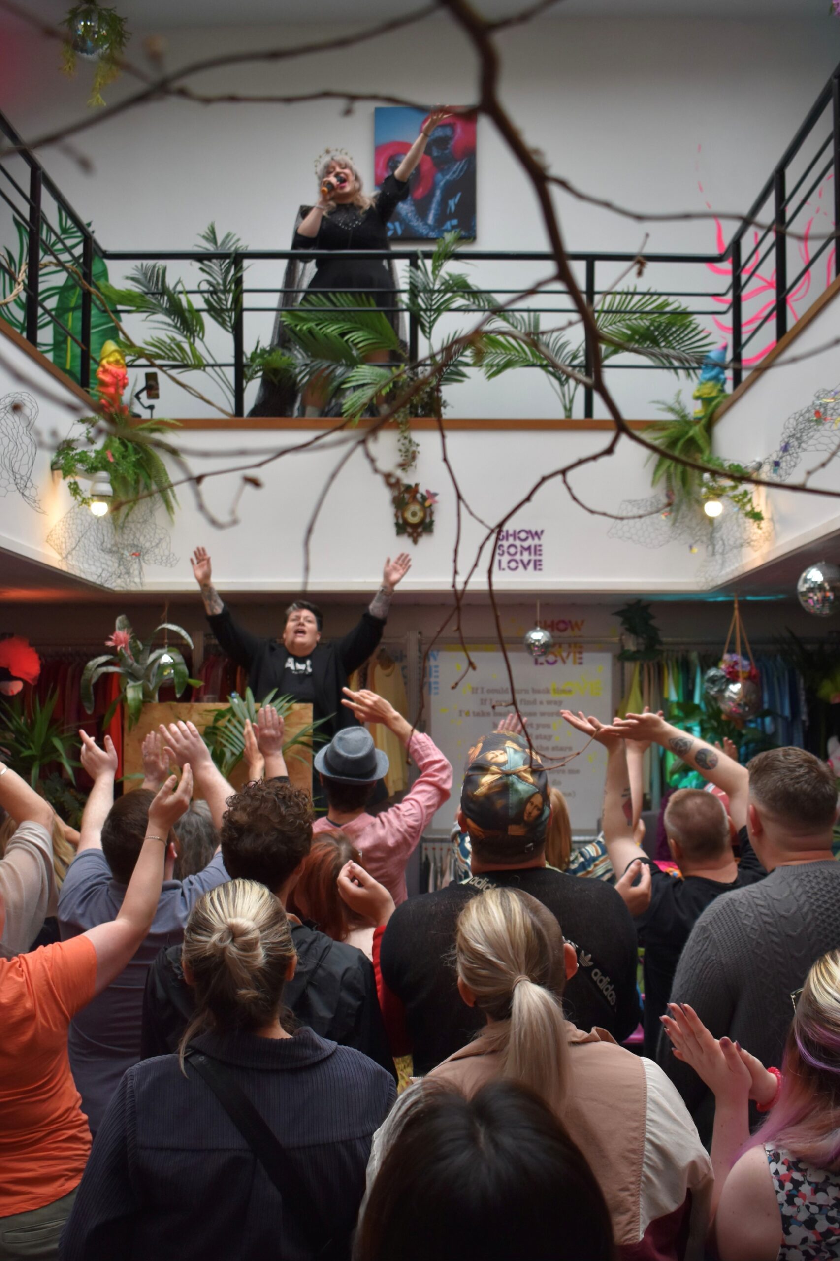 People with their hands in the air looking up at a singer performing on the balcony of the Green House at Show Some Love